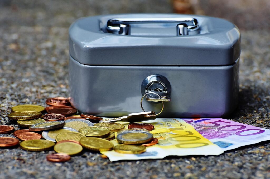 notas de dinheiro e moedas junto com um cofrinho com chave que representa uma reserva financeira de emergência